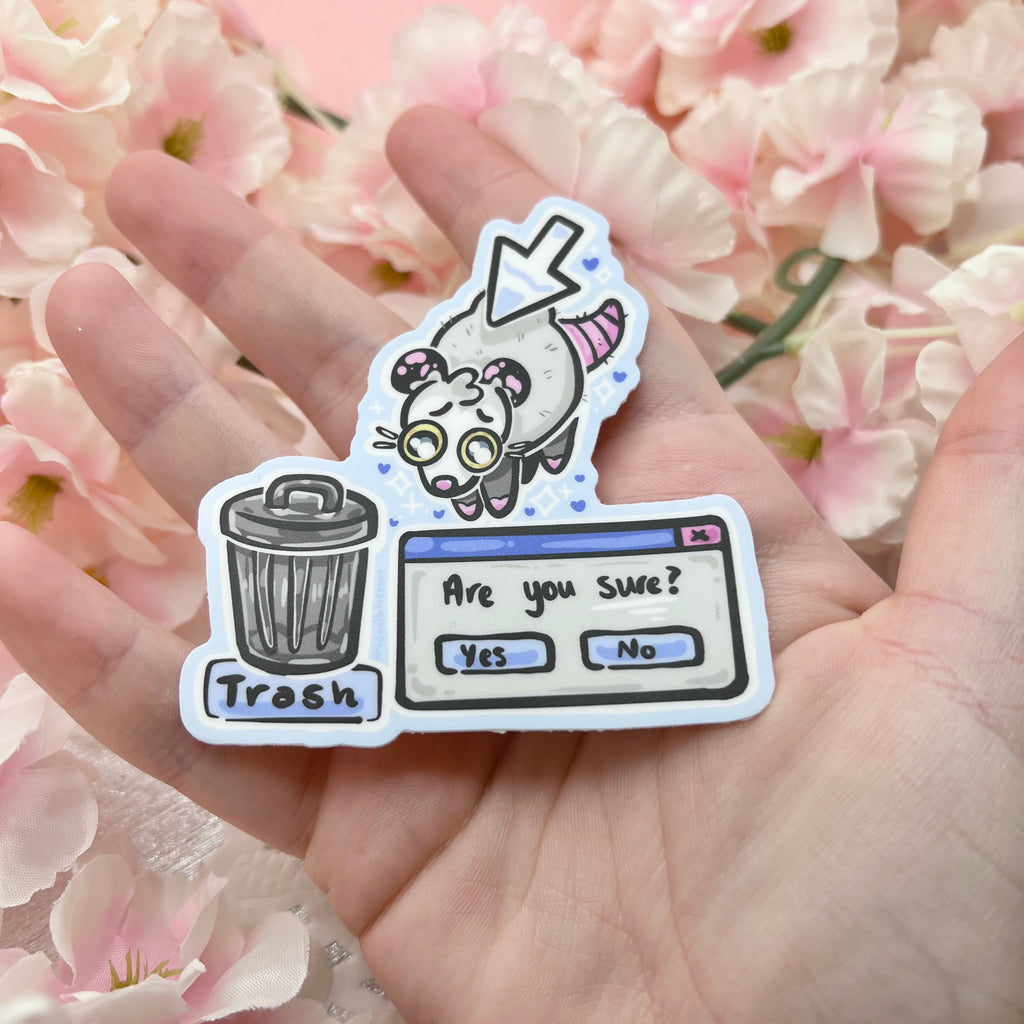 A sticker that features a cursor holding a fat opossum up, concerningly close to a trash can with a pop up asking if you're REALLY sure you want to drop him in.