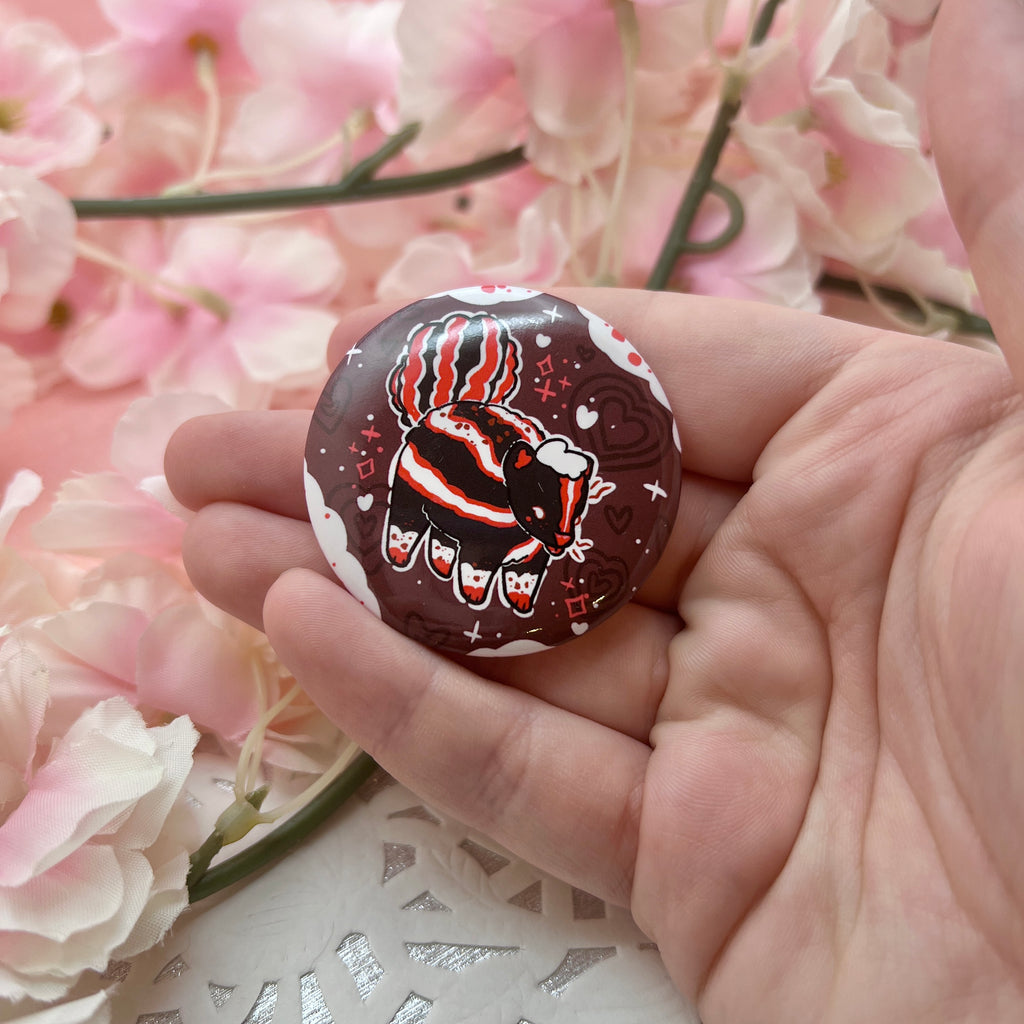 A button of a mostly normal skunk with red accents and chocolate spots, in front of a chocolate background