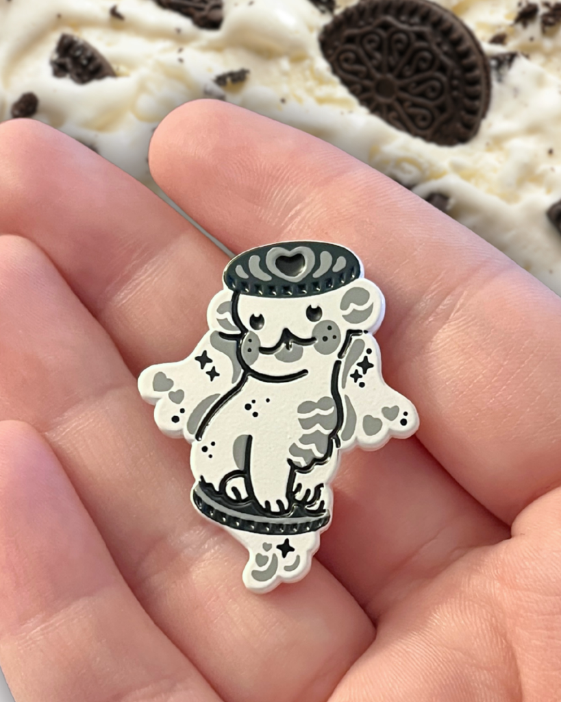 cookies and cream enamel pin dragon on a hand with cookies in the background