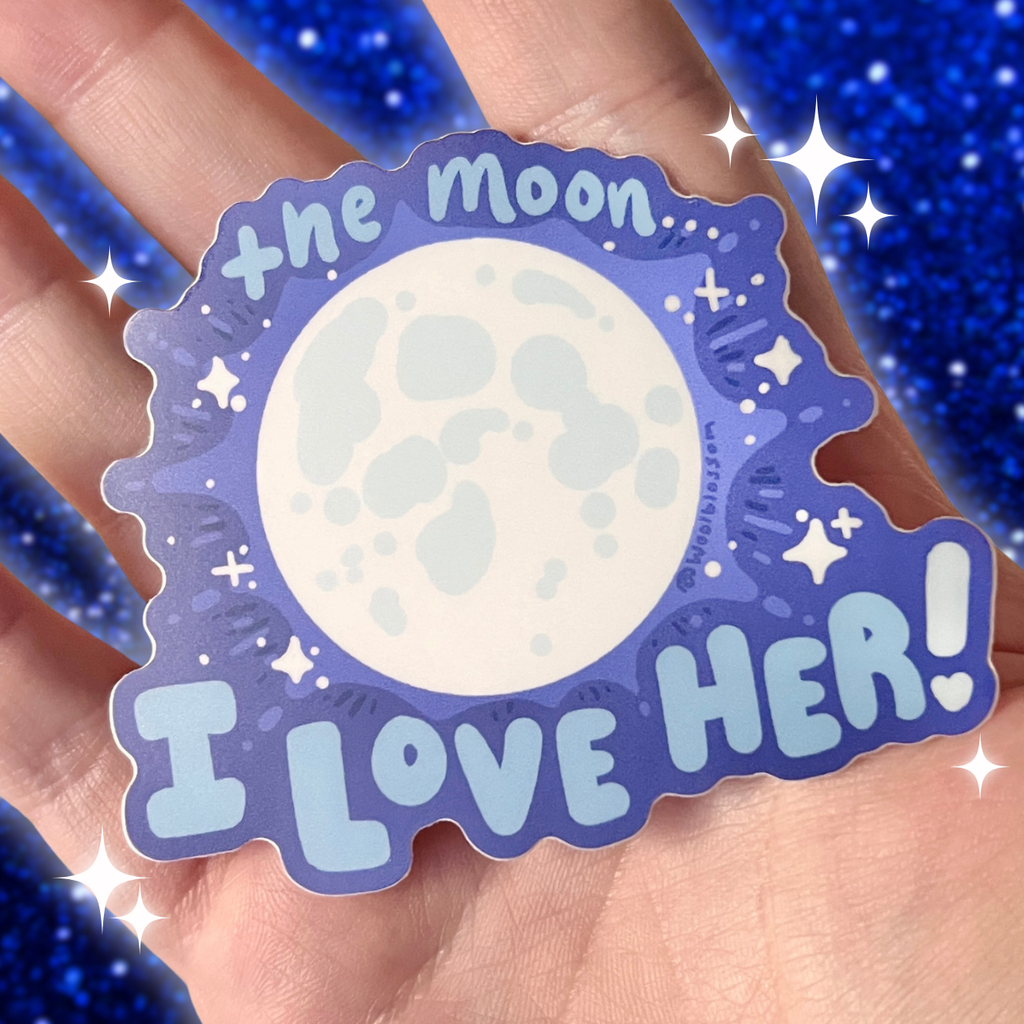 Sticker with moon design and 'I love her!' text held in hand against a blue glittery background