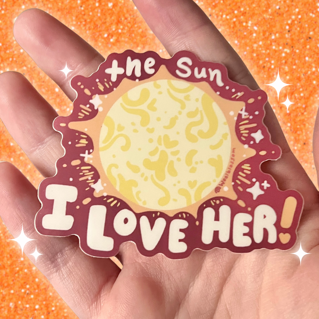 Sticker with sun design and text 'I Love Her' held in a hand against an orange glittery background