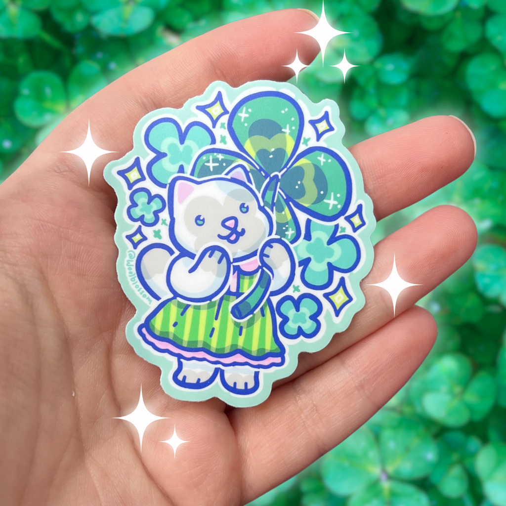 A sticker of a grey cat in a green stripe dress holding a four leaf clover