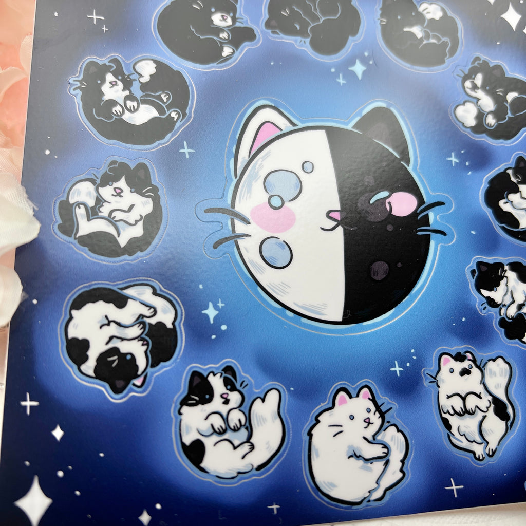  a sticker sheet of the phases of the moon that are made to look like different black to white cat coats- full moon is all white, quarter is a tuxedo, new moon is all black, etc.