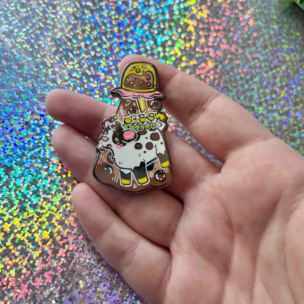 An alien boba cow being abducted by a boba enamel pin on a glitter background