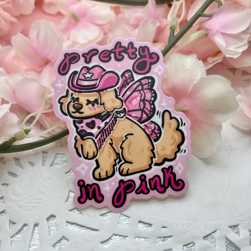 a sticker of a golden retreiver with a pink cowgirl hat, boots, and dark pink fairy wings and text that says "pretty in pink"