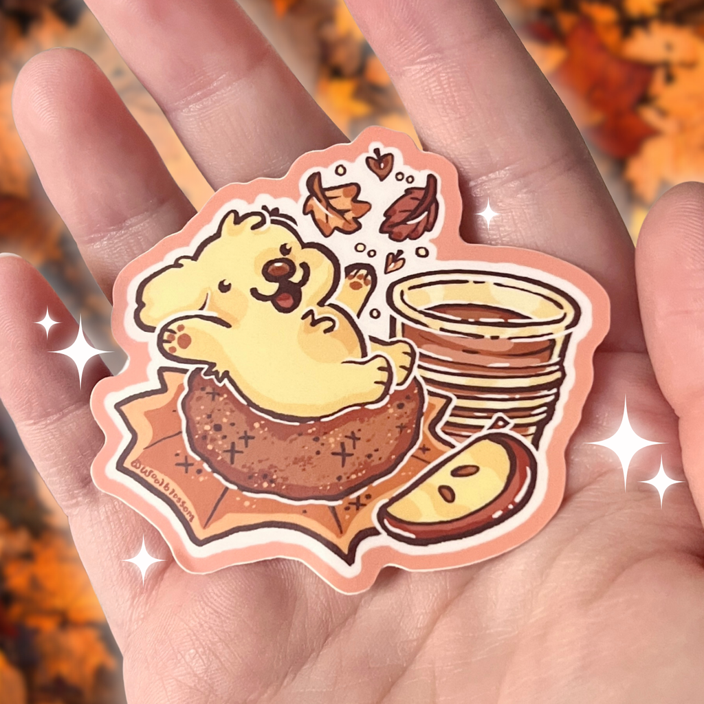 Sticker of a golden retriever on an apple doughnut held in a hand against an autumn leaf background