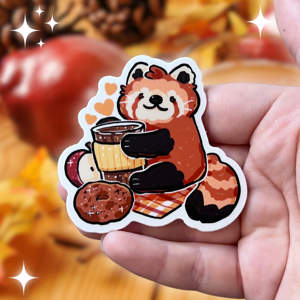 A sticker of a red panda holding a coffee drink with an apple, apple cider doughnut, on a warm toned plaid blanket