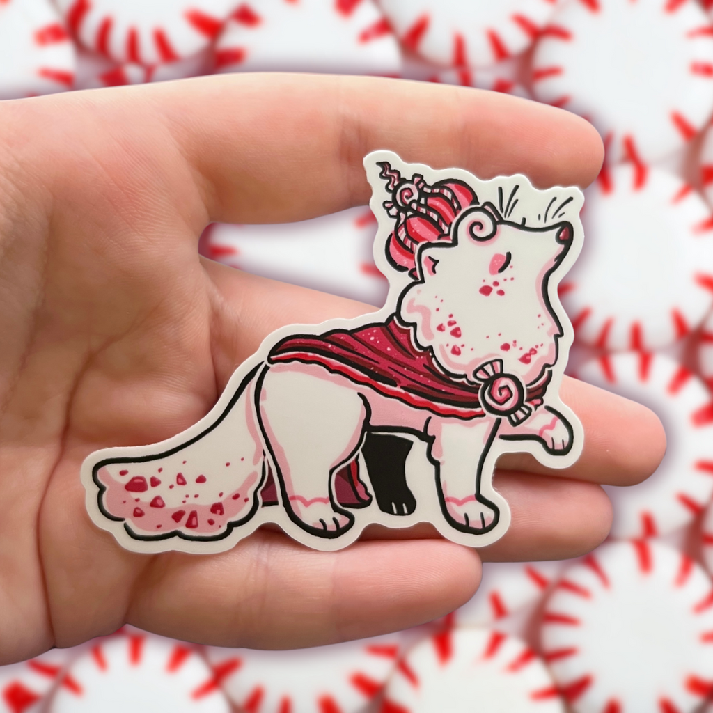 A sticker of a white fox with red specks, red robe, and red peppermint crown