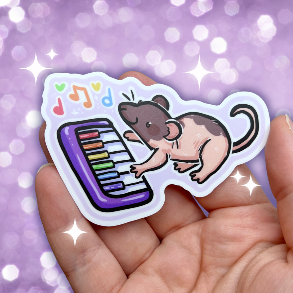 A sticker of a brown/pink mostly hairless rat playing a rainbow piano