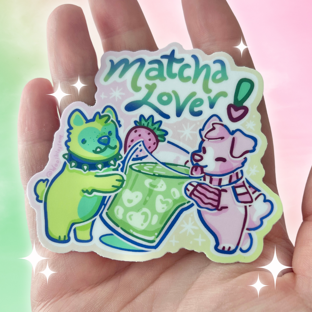 A sticker of a green dog and a pink dog sharing a cup of matcha, with text that says "matcha lover"