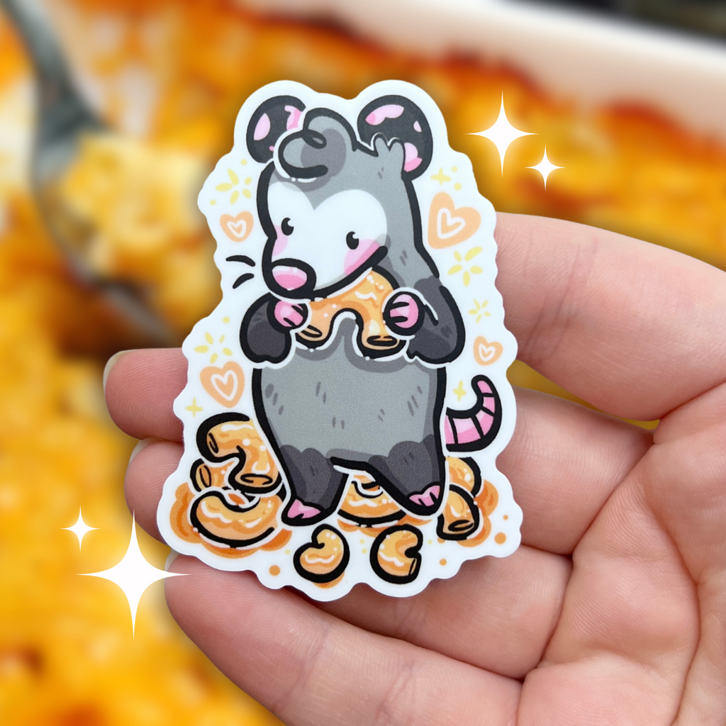 A sticker of an opossum standing in front of a pile of mac and cheese, holding one in its arms up to its mouth with hearts