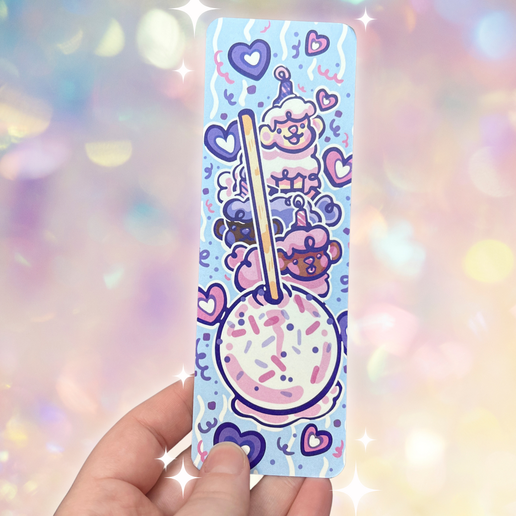 A bookmark of a confetti cakepop with three sheep stacked on top with candle hats