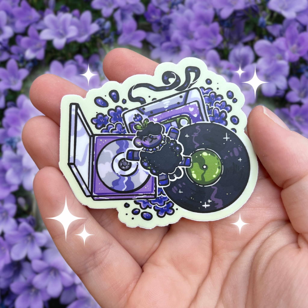 A sticker of violet, the dark and purple themed sheep laying happily on a pile of music media- a vinyl record, cassette, and CD, with purple flowers beneath them all