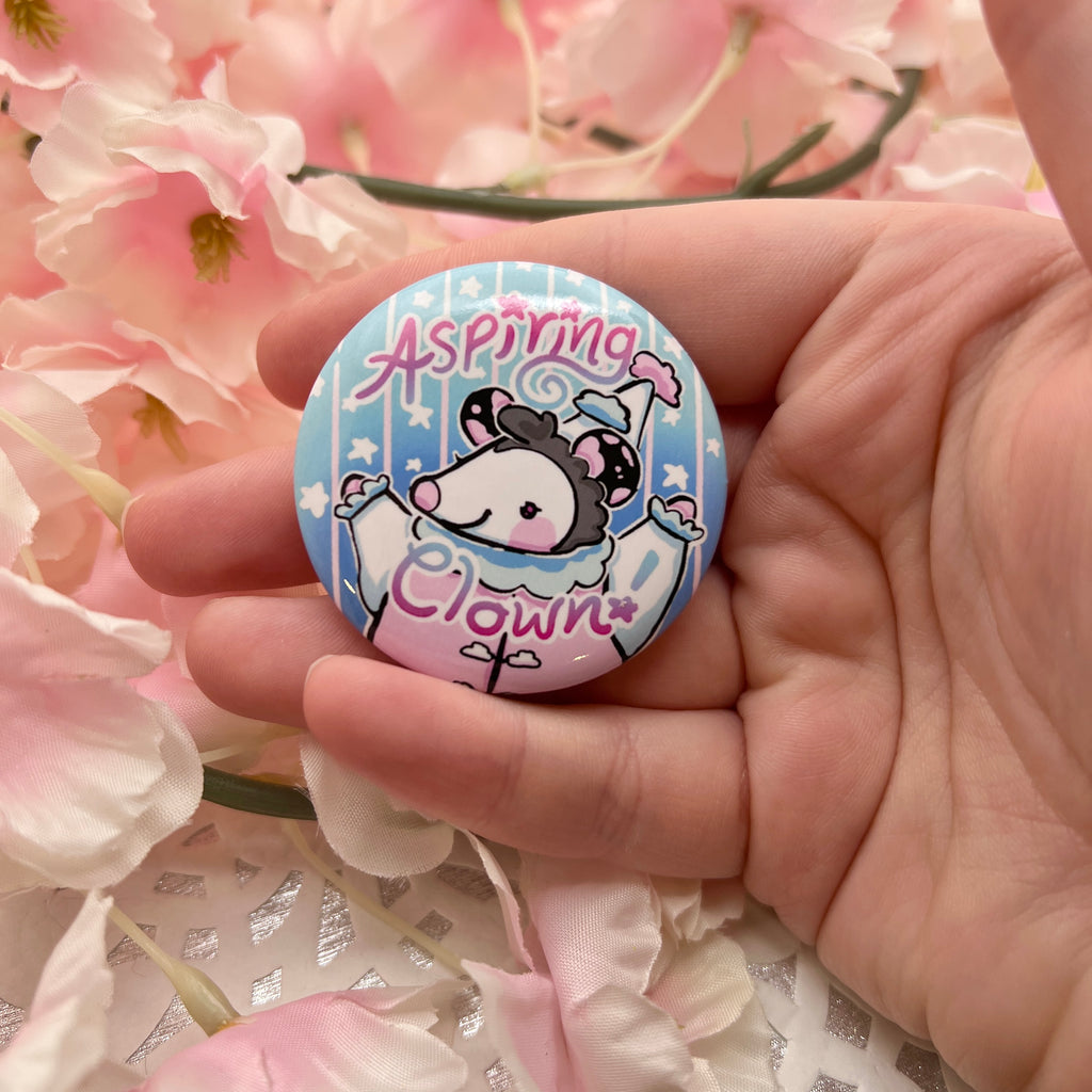 A button of a cloud themed opossum that looks happy with the text "aspiring clown"