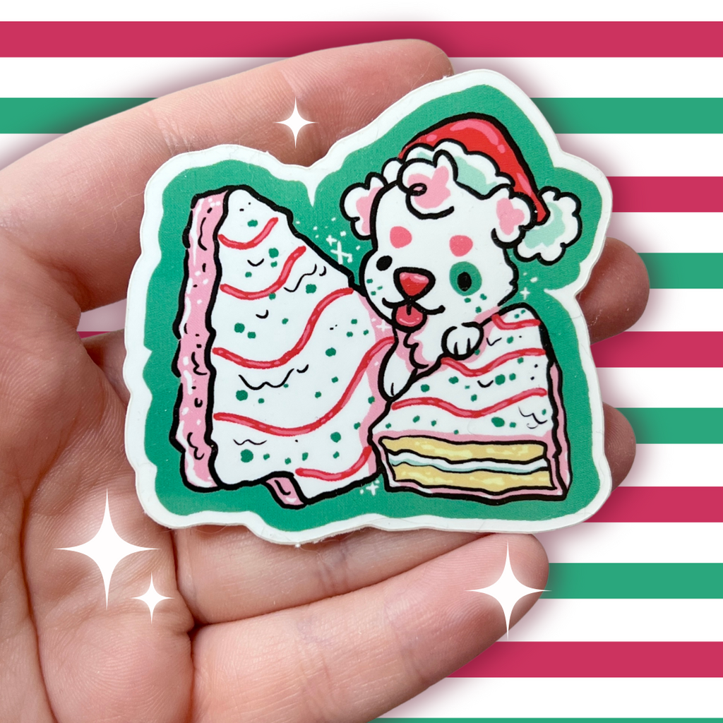 A sticker of a white puppy with a santa hat on top of two white christmas tree snack cakes