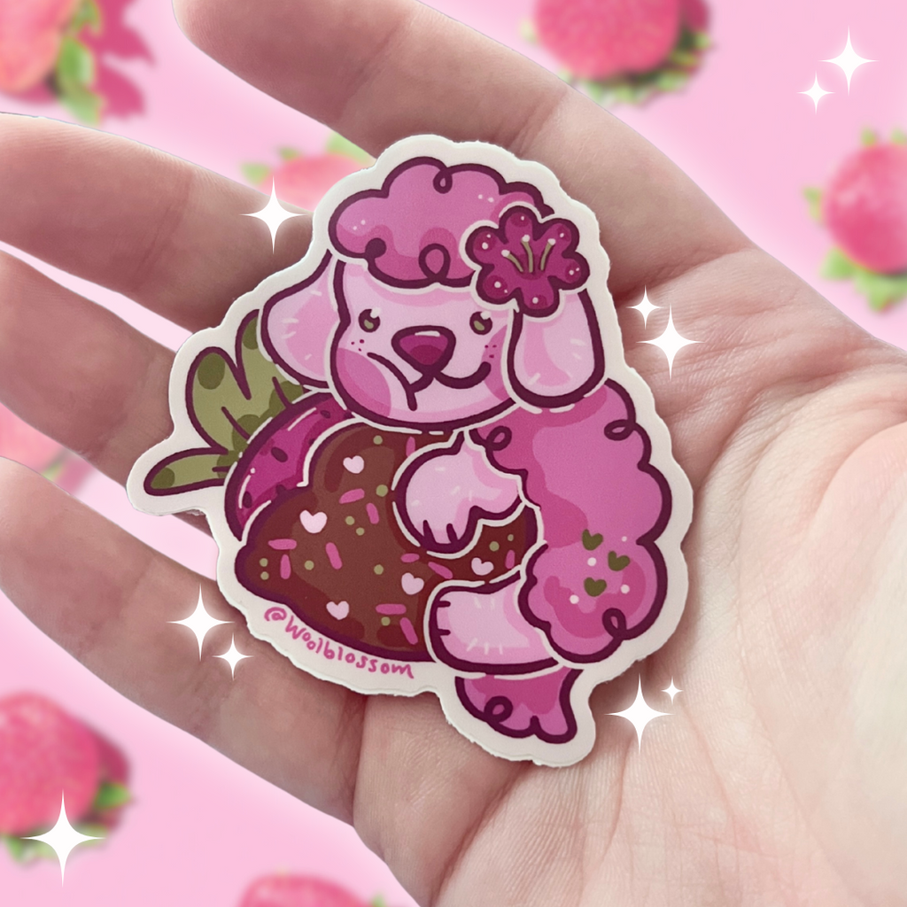Pink poodle on a strawberry sticker held in a hand with a pink background