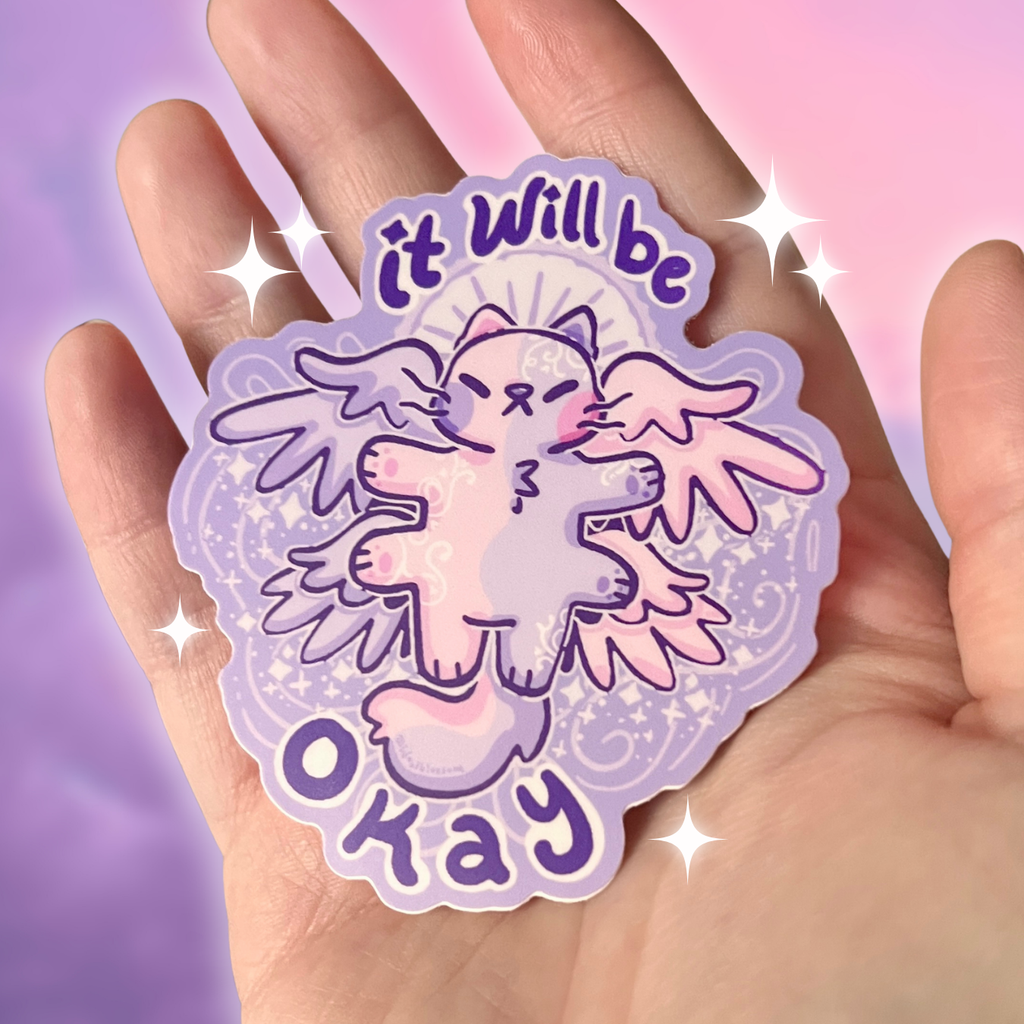 Sticker with a cartoon angel cat and 'it will be okay' text held in a hand against a pastel gradient background.