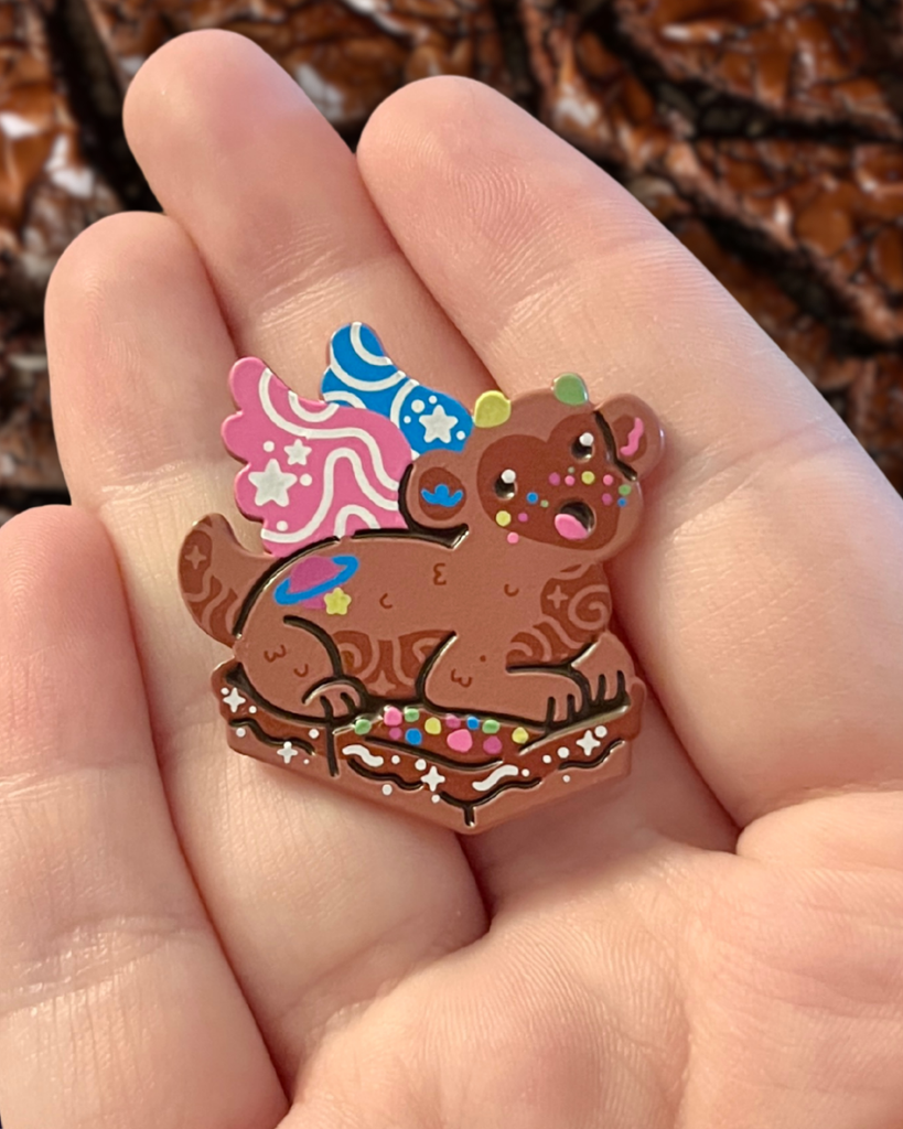 galaxy brownie dragon enamel pin held in a hand