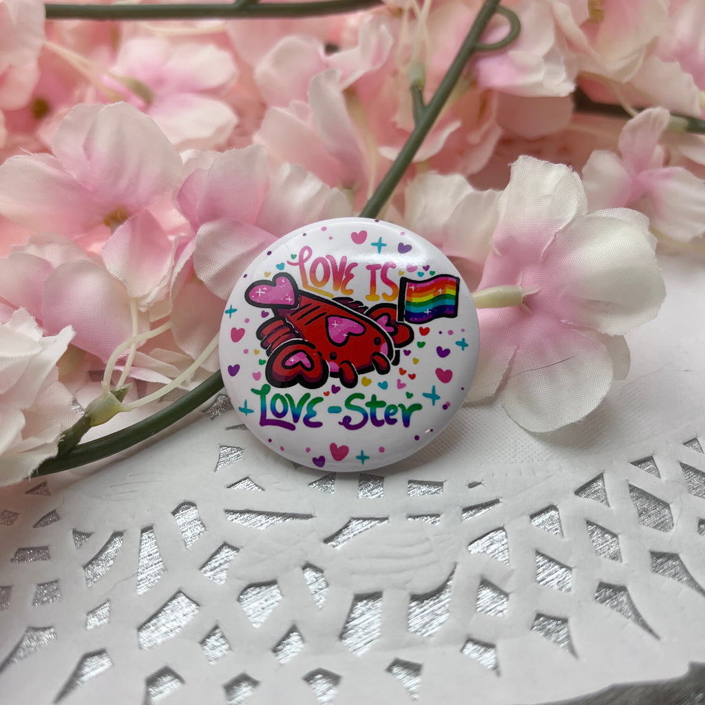 A button of a heart themed lobster holding a rainbow pride flag with text that says "love is love-ster"