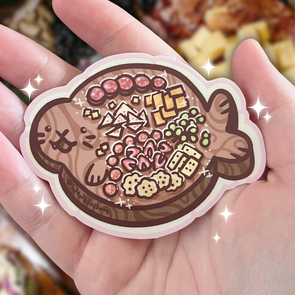 A sticker of a wooden board shaped like a seal with charcuterie foods on top
