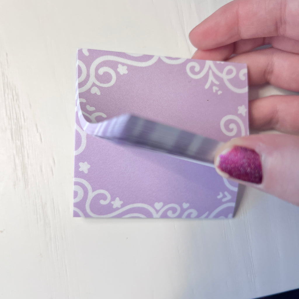 Hand holding a sticky note pad with white patterns against a white background