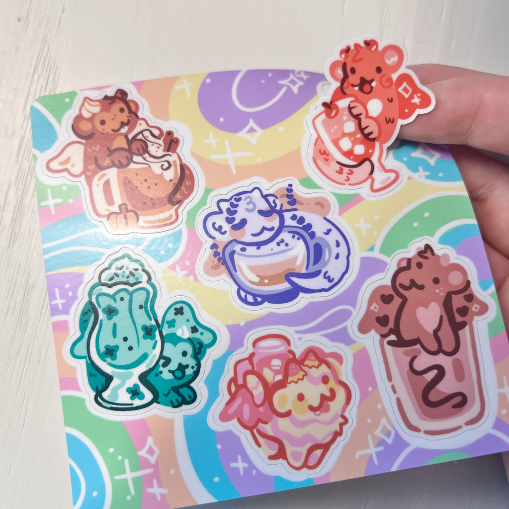 Set of colorful drink dragons on a sticker sheet held in a hand against a white background