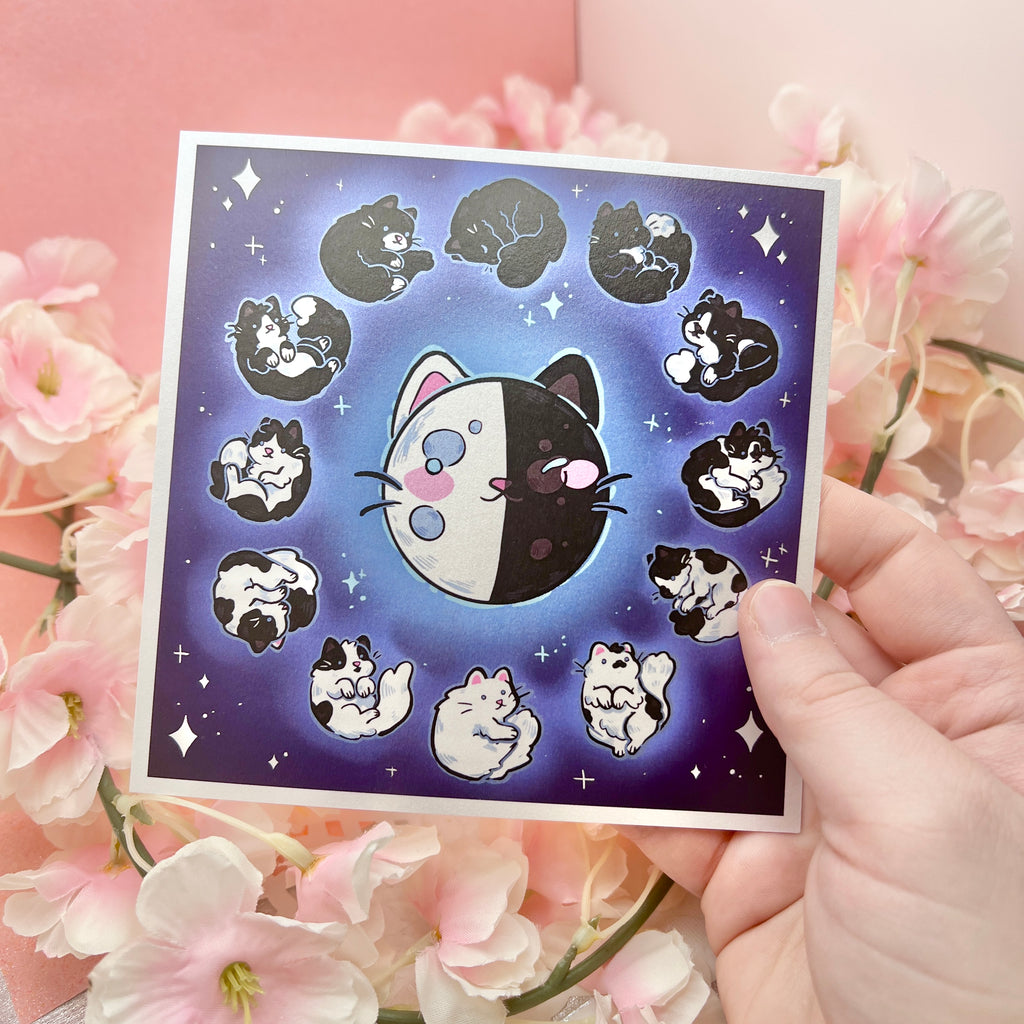  a print of the phases of the moon that are made to look like different black to white cat coats- full moon is all white, quarter is a tuxedo, new moon is all black, etc.