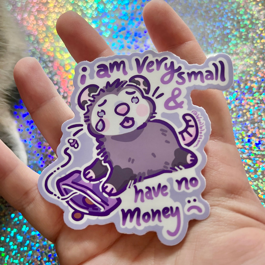hand holding Sticker of a sad opossum with text that says "i am very small and have no money" on a glittery background