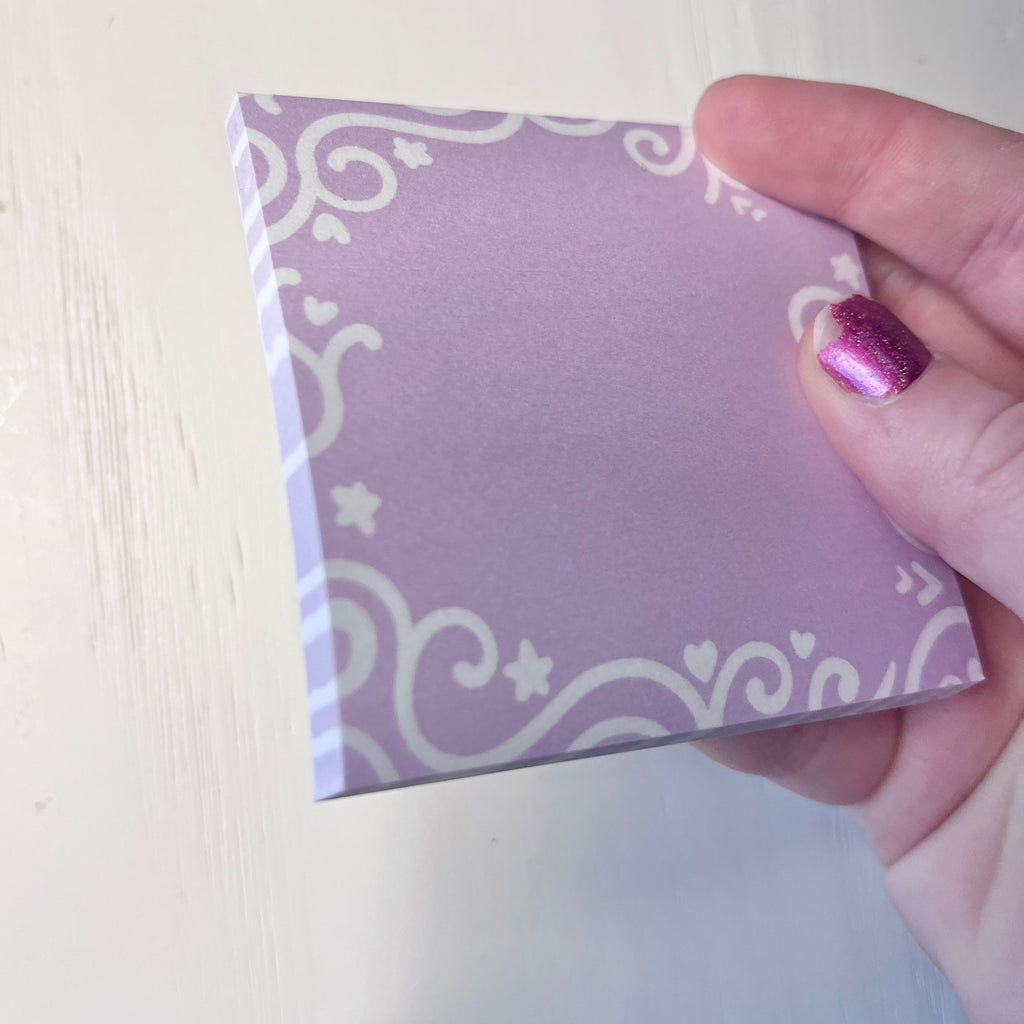 Hand holding a sticky note pad with white patterns against a white background