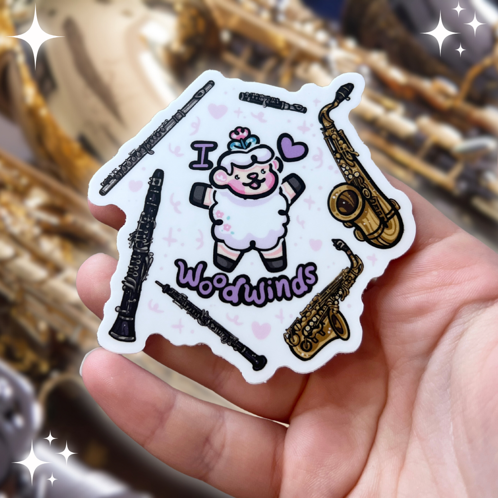 a sticker of a sheep with the text "I heart woodwinds" and six instruments floating around them (flute, piccolo, tenor sax, alto sax, oboe, clarinet)