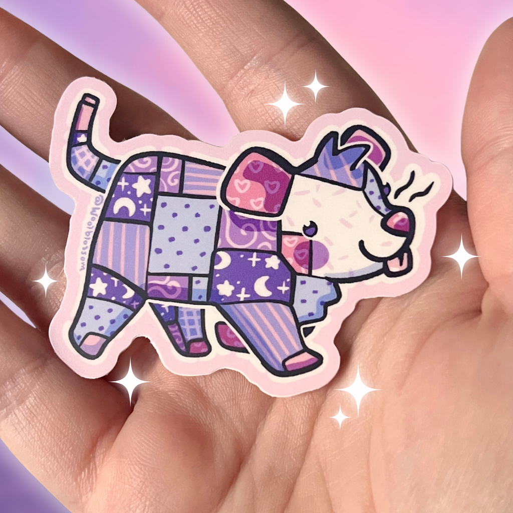 Sticker of a colorful patchwork opossum design held between fingers with a soft pink background