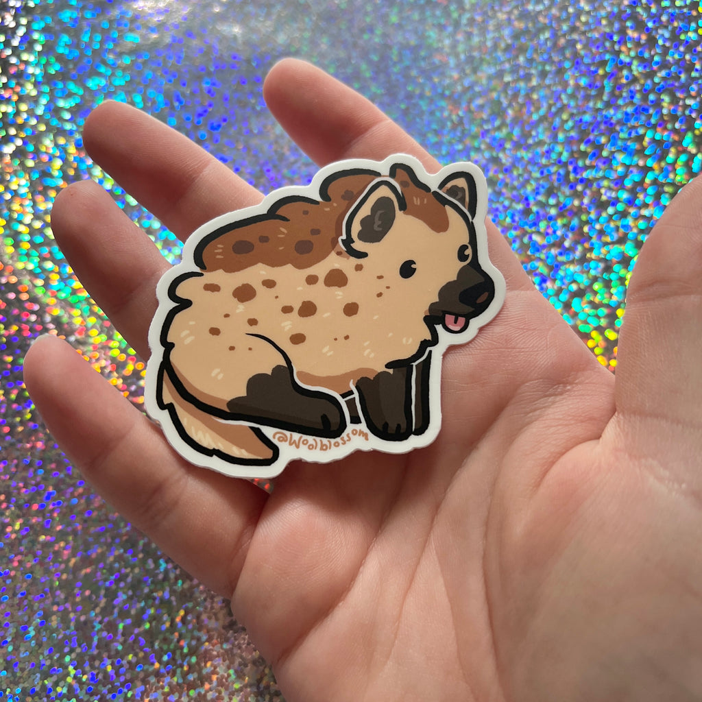 Hand holding a cartoon hyena sticker against a glittery background