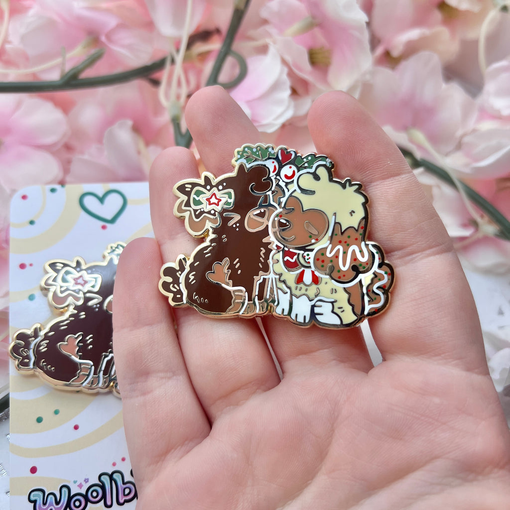 an enamel pin featuring Cinnamon, the Gingersnap puppy, and Caramel, the Sugar Cookie puppy, sharing a sweet mistletoe kiss