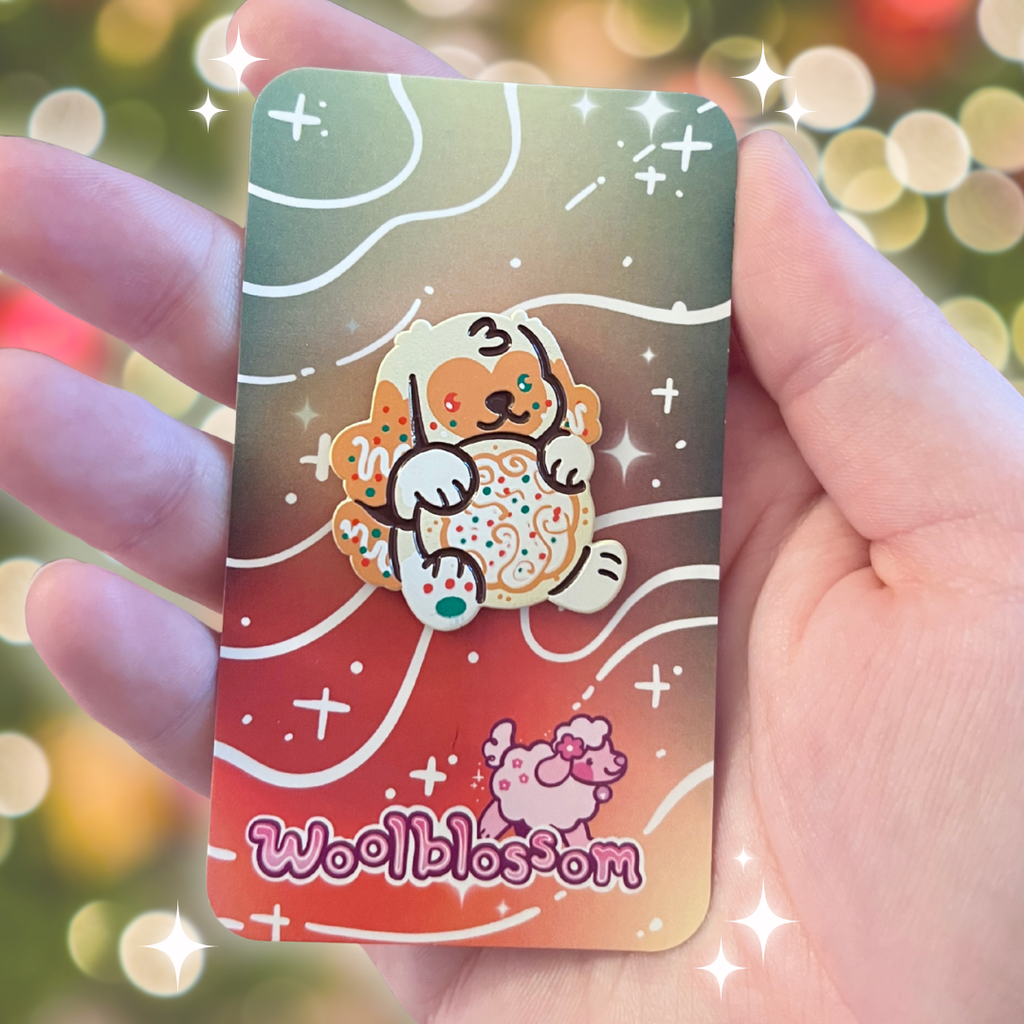 An enamel pin of a golden dog holding a sugar cookie