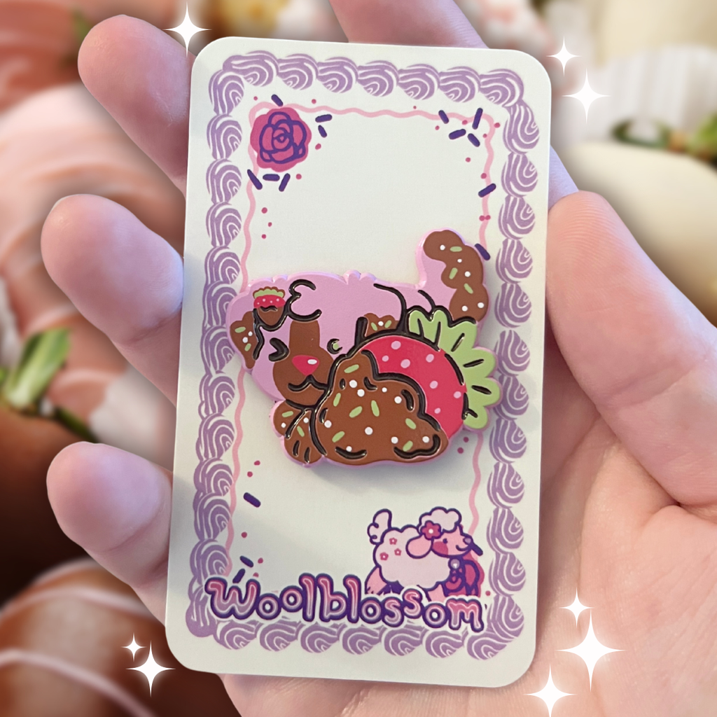 Enamel pin of a pink dog behind a chocolate strawberry