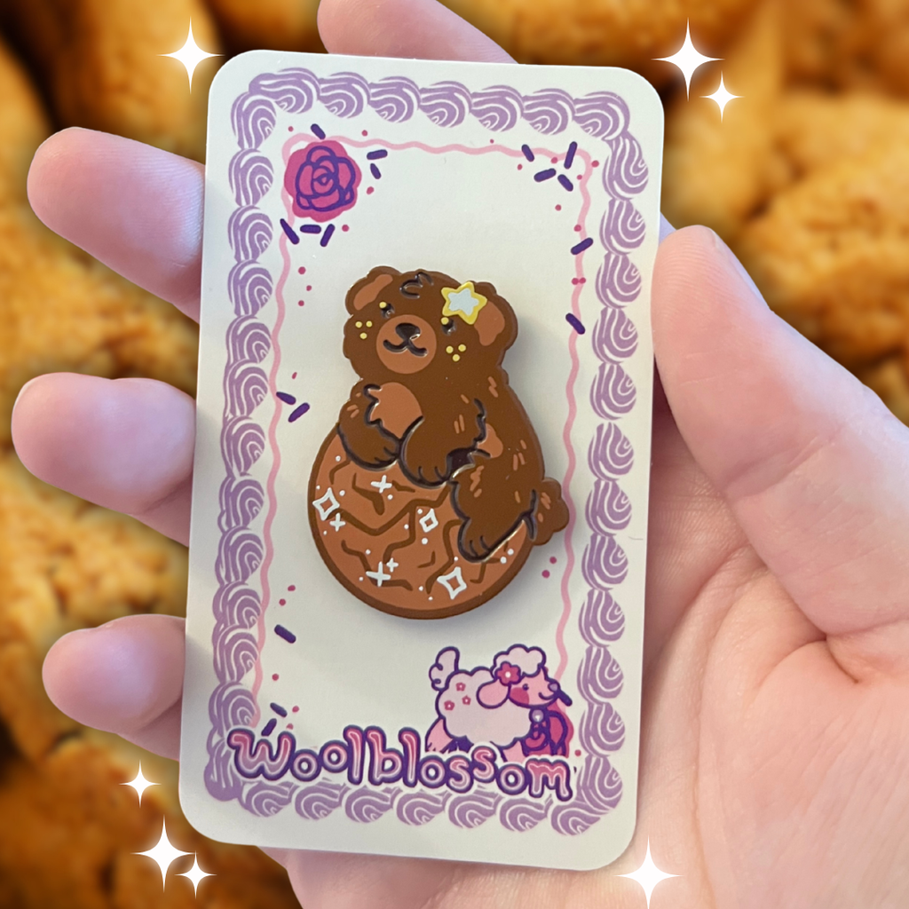An enamel pin of a brown fluffy dog on a ginger snap