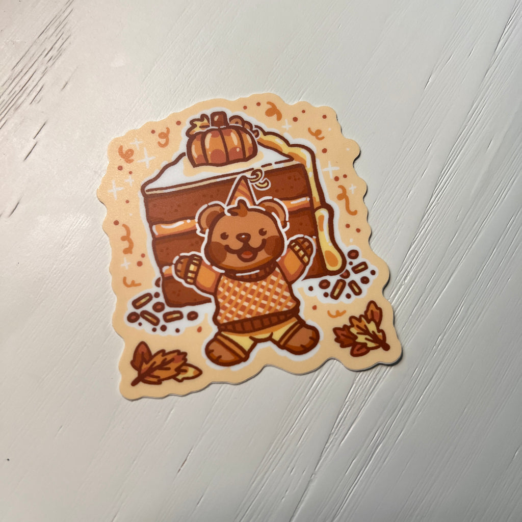 Sticker of a bear in an orange outfit with a pumpkin on top of a cake, on a white background