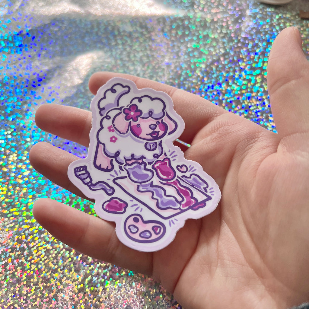 Hand holding Sticker of a cartoon puppy paw painting on a glittery background
