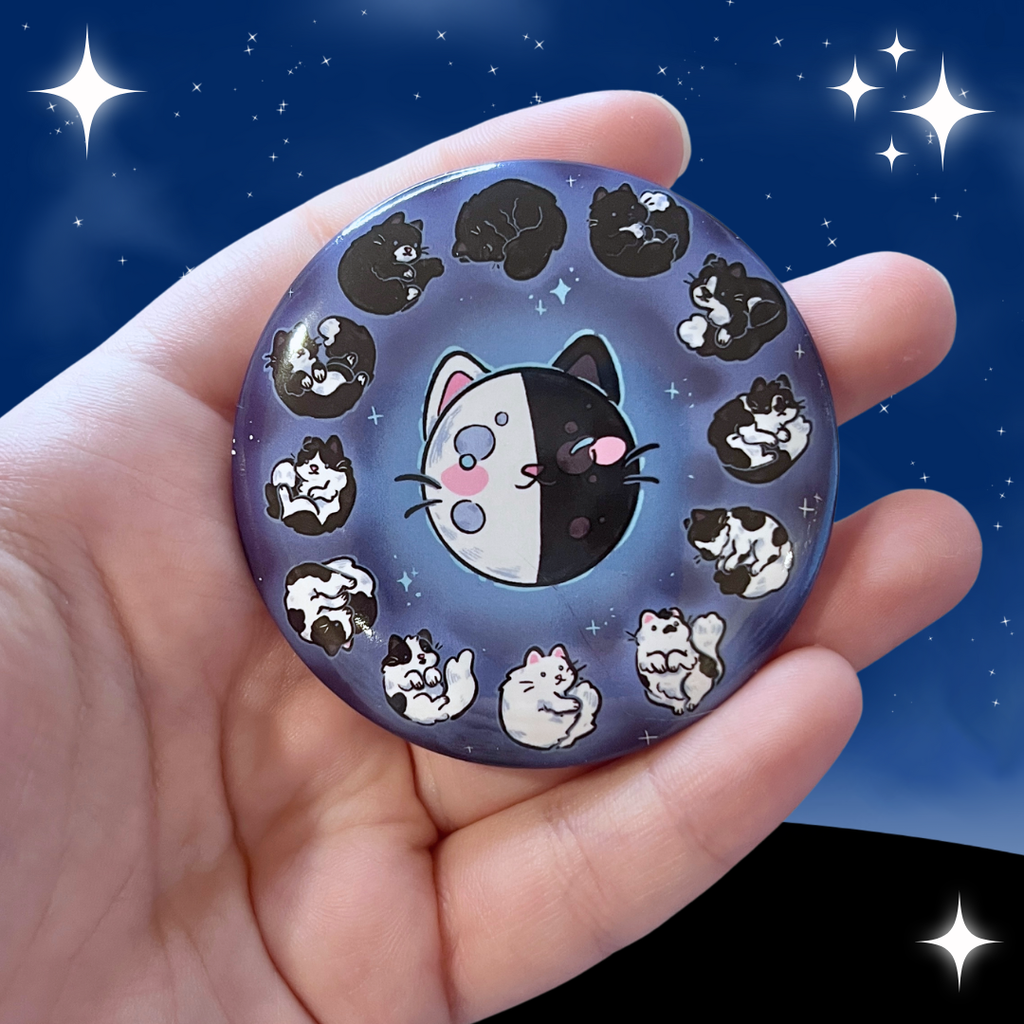  a button of the phases of the moon that are made to look like different black to white cat coats- full moon is all white, quarter is a tuxedo, new moon is all black, etc.