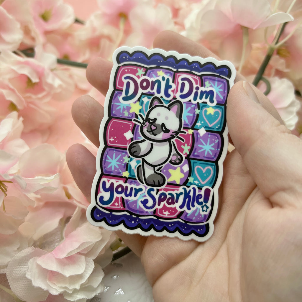 A cat walking with text that says "don't dim your sparkle!" on top of a purple quilt pattern