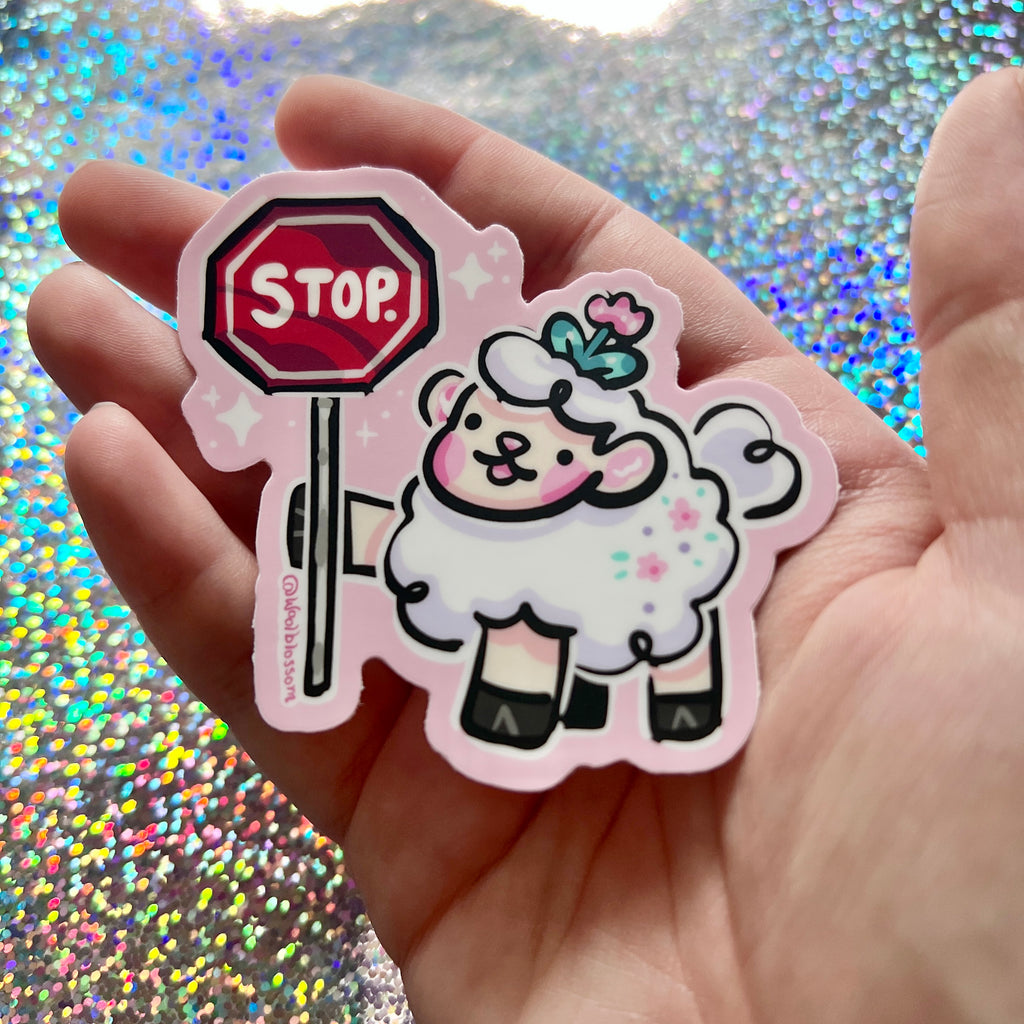 Hand holding a sticker of a sheep holding a stop sign against a glittery background.