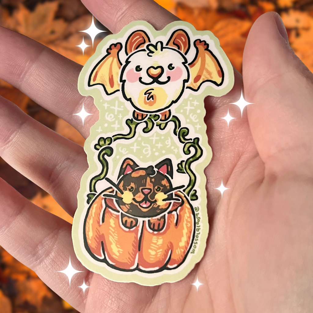 Halloween-themed sticker with a cat in a pumpkin and bat held by hands against a blurred autumn background.