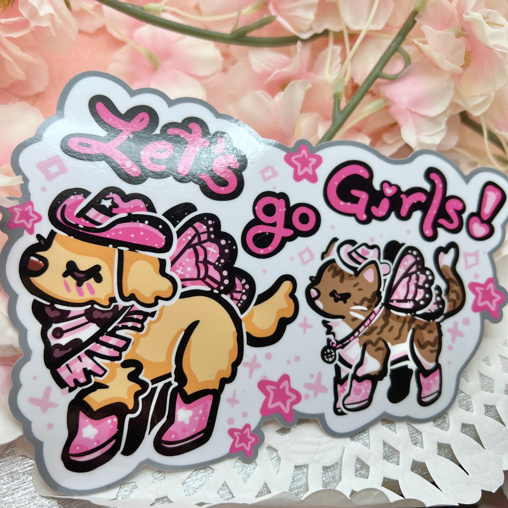 A bumper sticker of Two animals- one is a golden retreiver with a pink cowgirl hat, boots, and dark pink fairy wings. The second is a brown and white tabby cat with a white cowgirl haat, pink boots, and light pink butterfly wings. There is text that says "lets go girls!"