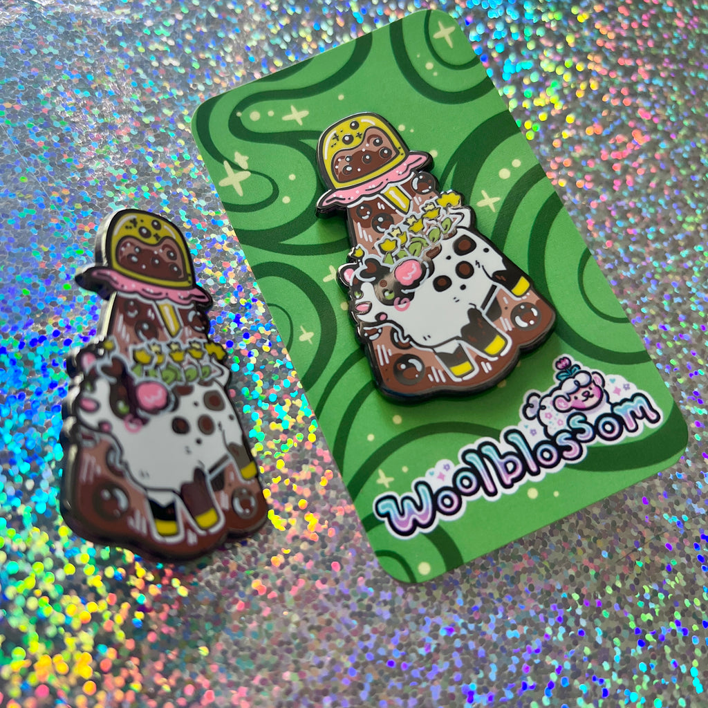 An alien boba cow being abducted by a boba enamel pin on a green card with 'Woolblossom' branding, on a glitter background