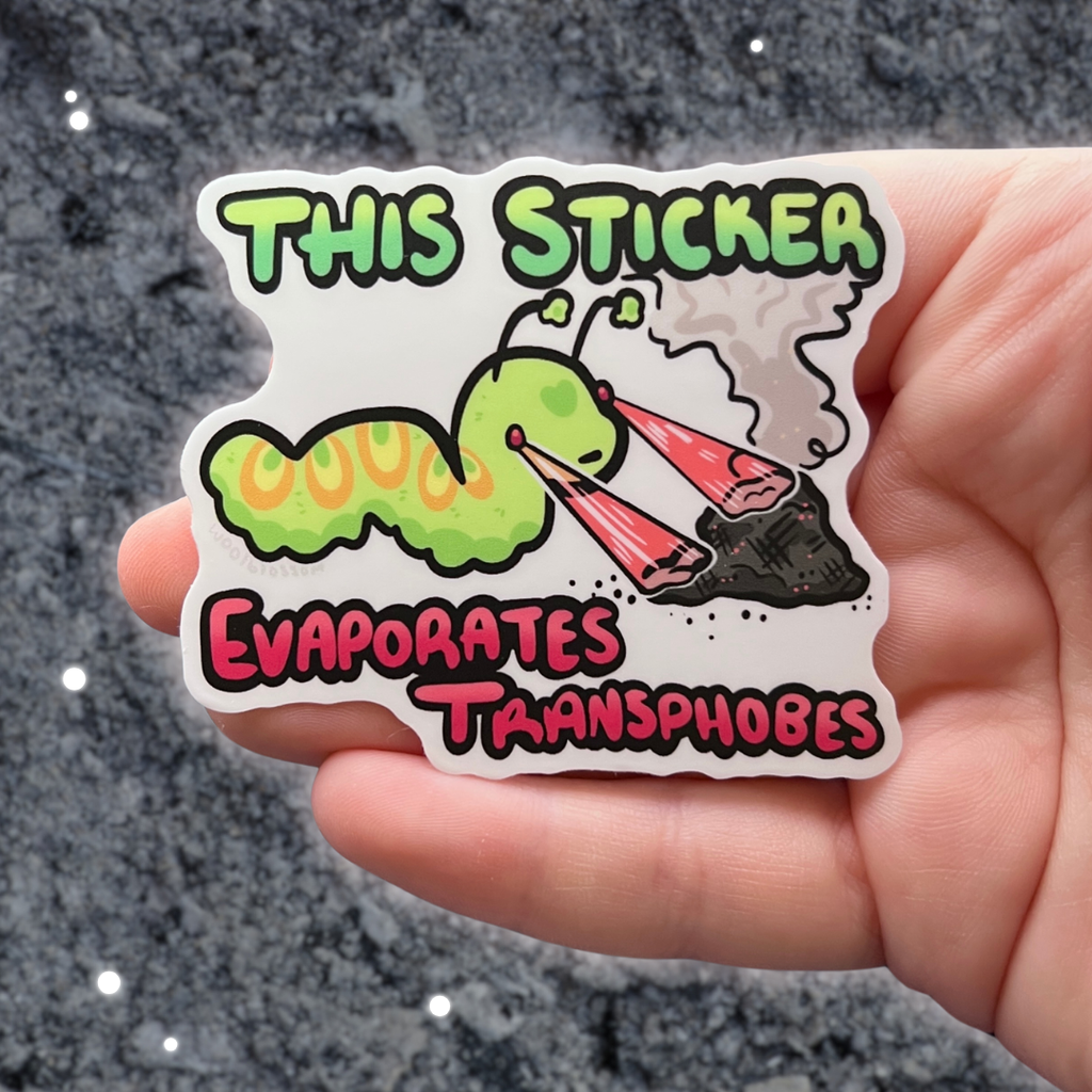 A sticker of a green worm shooting lasers out of its eyes onto a pile of ash with text that says "this sticker evaporates transphobes"