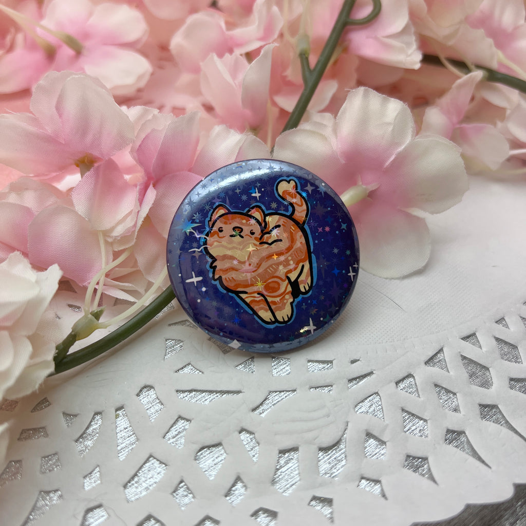 a button of an orange cat with markings like jupiter's