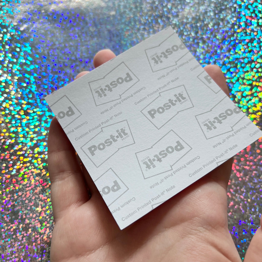 Hand holding back of a sheet of Post-it notes against a glittery background