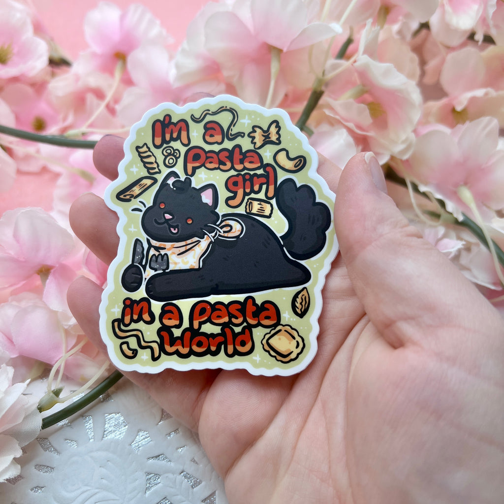 a sticker of a chonky black cat laying with a bib and utensils in hand, various pasta shapes floating around, with text that says "im a pasta girl, in a pasta world"