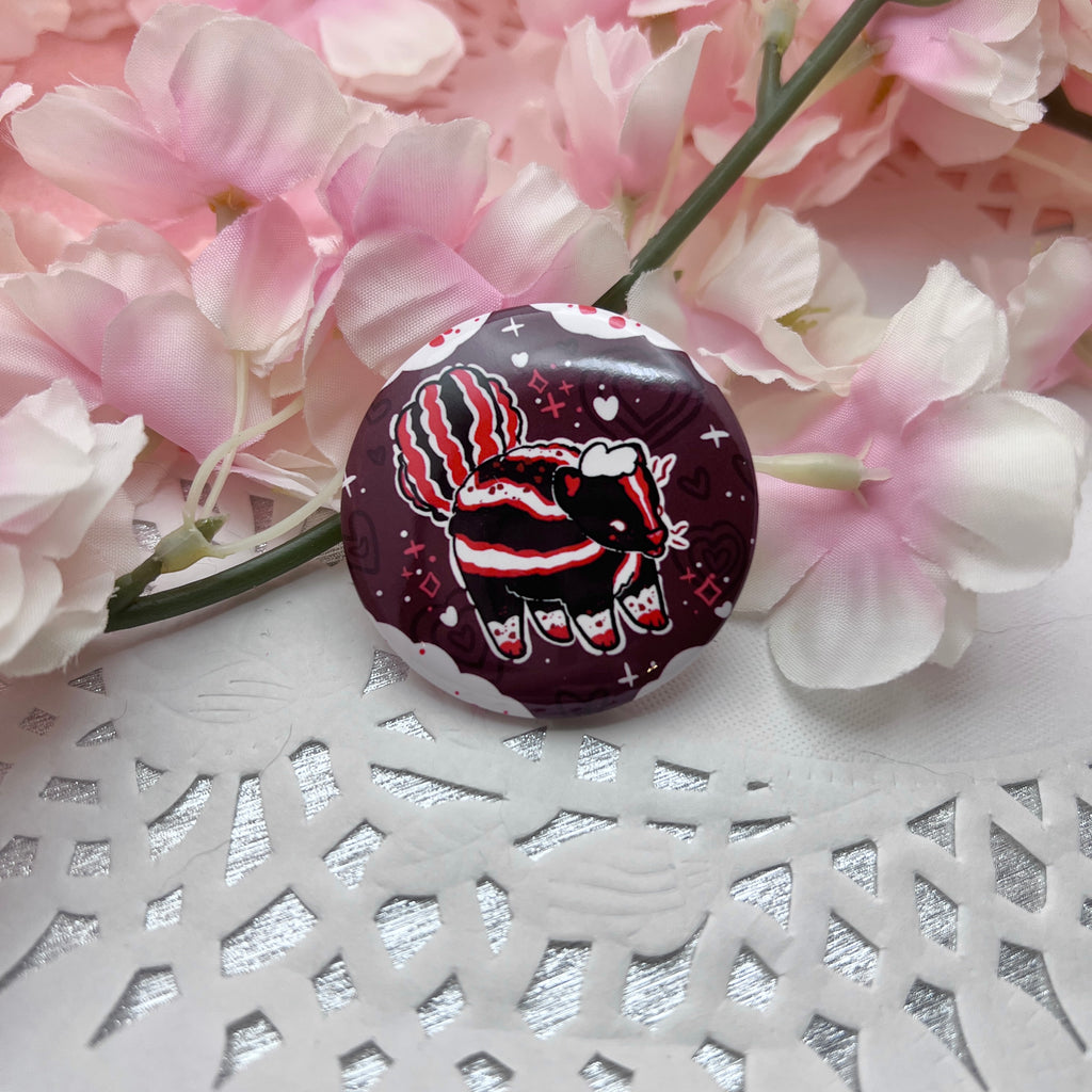 A button of a mostly normal skunk with red accents and chocolate spots, in front of a chocolate background