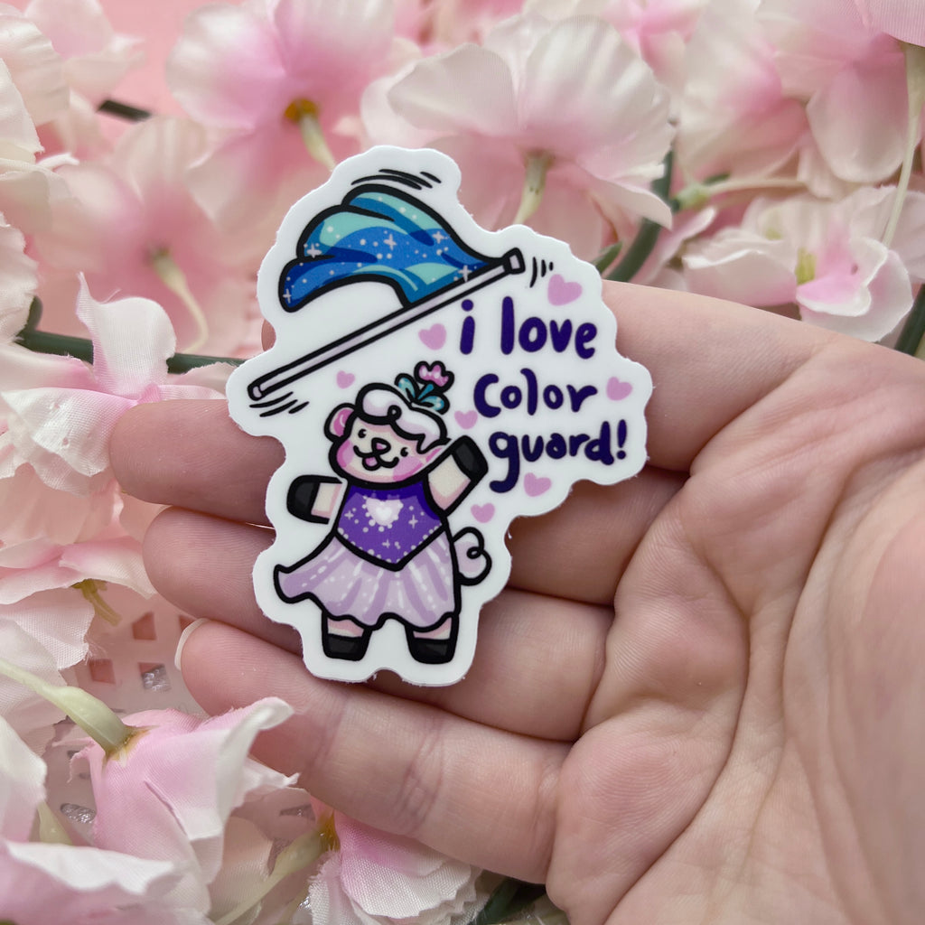 a sticker of sprout the sheep in a purple dress tossing a blue flag mid-air with the text "I love color guard"